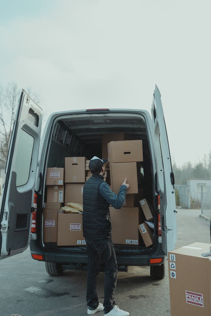 A delivery worker loading cardboard boxes into a van, preparing for shipment outdoors.