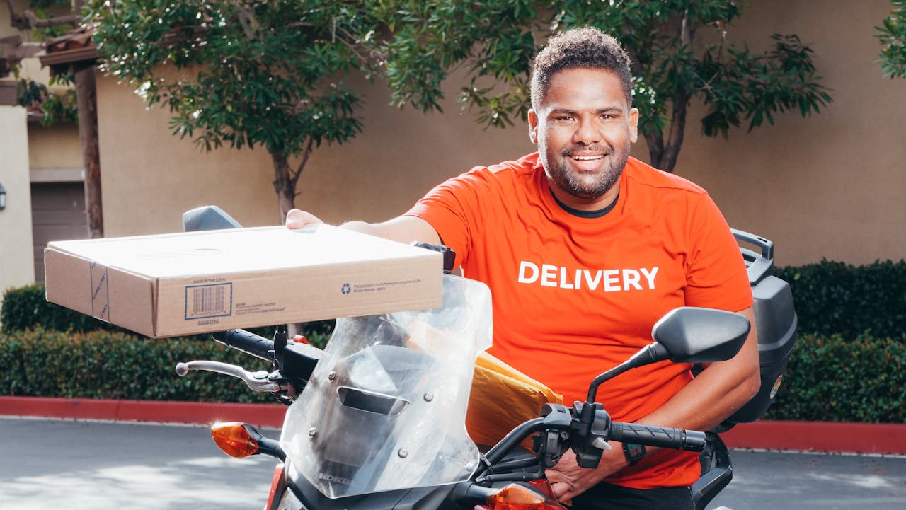 Smiling courier on a motorcycle carrying a package, ready for delivery.